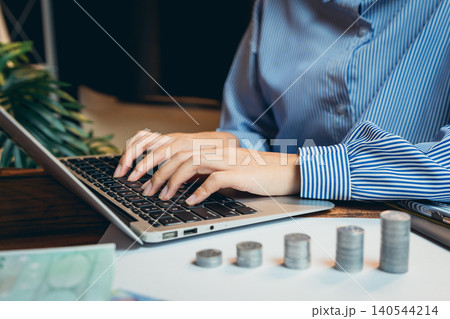 Business concept. Hands typing on laptop with coins arranged on desk, showcasing finance management and budgeting concepts Business concept. Hands typing on laptop with coins arranged on desk, showcasing finance management and budgeting concepts 140544214