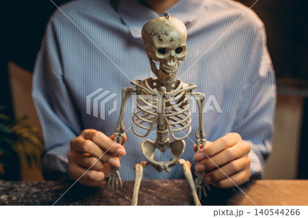 Halloween prop concept. Human Skeleton Model Held by a Person in Striped Shirt for Educational and Artistic Purposes 140544266