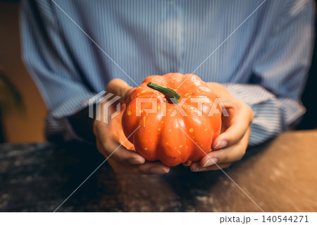 Halloween prop concept. Person Holding a Bright Orange Pumpkin Against a Dark Background in a Cozy Indoor Setting 140544271