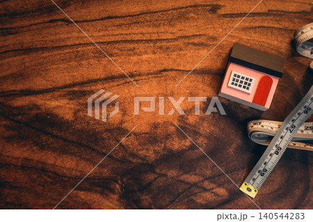 The concept of buying a house. Small wooden house model with a measuring tape on a rustic wooden surface for home improvement projects The concept of buying a house. Small wooden house model with a measuring tape on a rustic wooden surface for home improvement projects 140544283