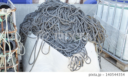 Thick grey mooring ropes are stored in a white plastic container at a commercial port. This location supports the fishing and maritime industries in daily operations. 140544354