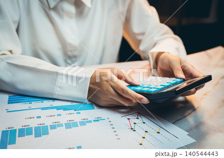 Business concept. Business analysis and financial calculation with mobile device and charts on table during late night work session Business concept. Business analysis and financial calculation with mobile device and charts on table during late night work session 140544443