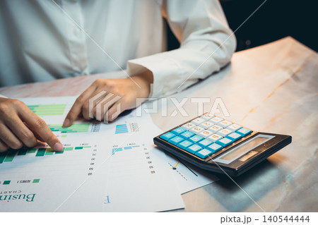 Business concept. Person Analyzing Financial Data with Calculator and Charts for Business Planning and Budgeting Tasks Business concept. Person Analyzing Financial Data with Calculator and Charts for Business Planning and Budgeting Tasks 140544444