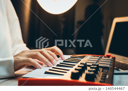 Pianist Concept. Hands Playing Keys on Electronic Musical Instrument with Laptop and Soft Light in Modern Home Studio Setting Pianist Concept. Hands Playing Keys on Electronic Musical Instrument with Laptop and Soft Light in Modern Home Studio Setting 140544467
