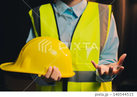 Engineer concept. Construction Worker in Safety Vest Holding Yellow Hard Hat with Outstretched Hand Presenting Information Engineer concept. Construction Worker in Safety Vest Holding Yellow Hard Hat with Outstretched Hand Presenting Information 140544515