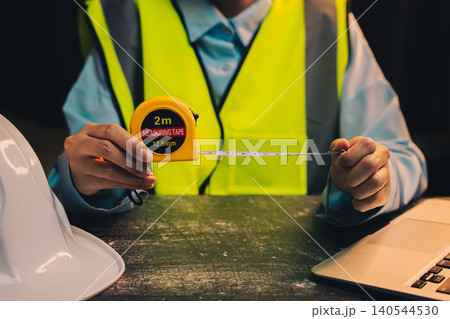 Engineer concept. Construction Professional in Safety Vest Using Measuring Tape for Accurate Measurements on Worksite Engineer concept. Construction Professional in Safety Vest Using Measuring Tape for Accurate Measurements on Worksite 140544530