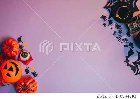 Halloween flat lay. Colorful Halloween Decorations with Pumpkins, Spiders, and Festive Props on a Purple Background Halloween flat lay. Colorful Halloween Decorations with Pumpkins, Spiders, and Festive Props on a Purple Background 140544593