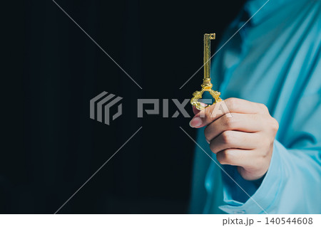 Success key concept. Elegant hand holding a vintage golden key against a dark background, symbolizing secrets and opportunities Success key concept. Elegant hand holding a vintage golden key against a dark background, symbolizing secrets and opportunities 140544608