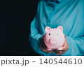 Businessman Holding Pink Piggy Bank Against Dark Background for Saving Money and Financial Planning Concept 140544610