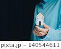 Businessman Holding Small Model House with Blue Shirt in Dark Background Representing Home and Real Estate Concept 140544611
