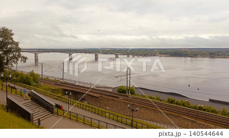 Urban Riverfront Landscape with Concrete Bridge, Train Tracks, and Pedestrian Walkway under Cloudy Sky Urban Riverfront Landscape with Concrete Bridge, Train Tracks, and Pedestrian Walkway under Cloudy Sky 140544644