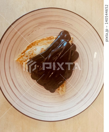 Folded Crepes Covered with Thick Chocolate Sauce on a Striped Plate Top View 140544652