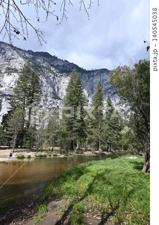 Tranquil mountain stream flowing through green meadows beneath massive cliffs. 140545038