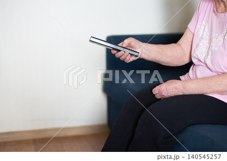 Senior woman holding remote control watching tv at home Senior woman holding remote control watching tv at home 140545257