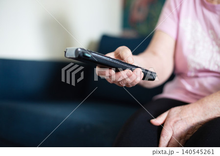 Senior woman with remote controller at home switching channels watching TV 140545261