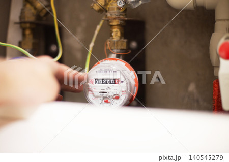 Hand checking water meter reading for utility consumption Hand checking water meter reading for utility consumption 140545279