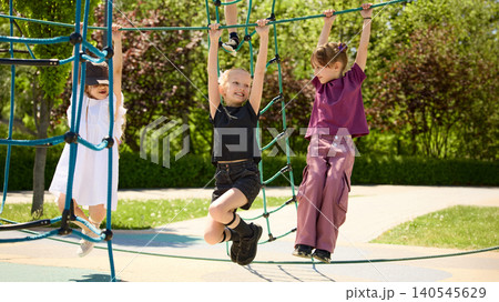 Children climbing rope playground equipment together in sunny park. 140545629