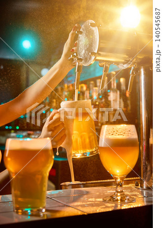 Female bartender pouring foamy draft beer beside glowing pub glasses. Female bartender pouring foamy draft beer beside glowing pub glasses. 140545687