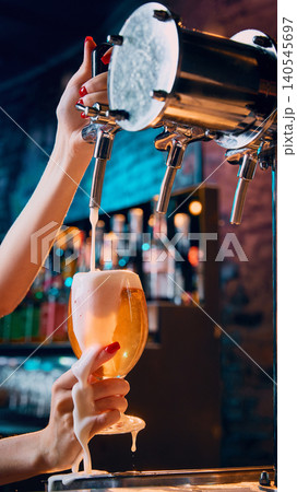 Female hand serving draft beer with thick foam in dim bar Female hand serving draft beer with thick foam in dim bar 140545697