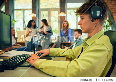 Young designer working with headphones at computer in creative office. Young designer working with headphones at computer in creative office. 140545860