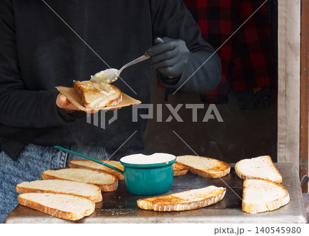 Cook spreading savory topping on grilled sourdough street food at Naplavka market 140545980