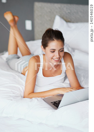 Woman, lying and laptop with smile in bed for connection, typing and chatting to friends, Female person, technology and computer for conversation in casual outfit, and comfortable in bedroom or home 140546019