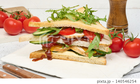 Multilayer sandwich with chicken, fresh cucumber, tomato and arugula, topped with sauce on white background. 140546254
