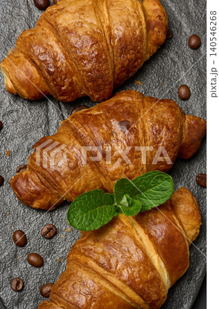 Golden croissants lined up on a dark stone board with a sprig of mint. Top view. Golden croissants lined up on a dark stone board with a sprig of mint. Top view. 140546268