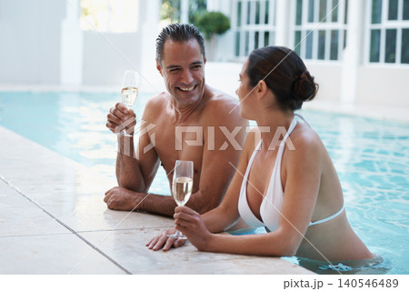 Champagne, hotel and couple relax in pool for swimming, man and woman together with happiness for honeymoon. Resort, female person and guy smile for love in marriage, bonding and girl with bikini 140546489