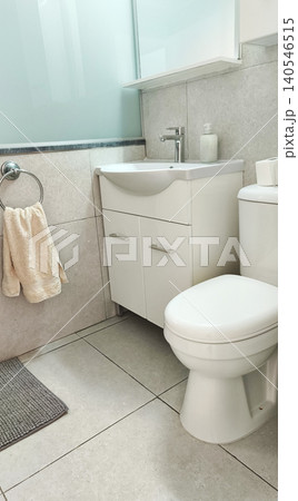 Vertical view of a modern clean bathroom featuring a toilet, sink vanity, soft towel, and tiled walls. Bright minimalist interior with a fresh, hygienic, and comfortable atmosphere. Vertical view of a modern clean bathroom featuring a toilet, sink vanity, soft towel, and tiled walls. Bright minimalist interior with a fresh, hygienic, and comfortable atmosphere. 140546515