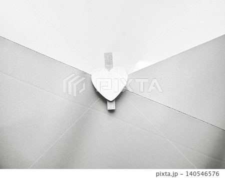 wooden heart clothespin clipped to white envelope flap in minimalist monochrome closeup with soft shadows 140546576