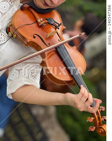 Violin woman player performs live music outdoors, with violin and bow captured close up, cultural performance. Classical music, city live music, musician hands, string instrument, event promotion 140547366