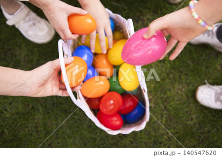 Colorful plastic Easter eggs being held by multiple hands above a basket filled with various colored eggs on green grass during an outdoor spring celebration Colorful plastic Easter eggs being held by multiple hands above a basket filled with various colored eggs on green grass during an outdoor spring celebration 140547620