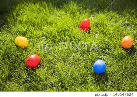 Colorful plastic Easter eggs in red, yellow, orange, and blue scattered on vibrant green grass during a sunny day, ideal for festive spring celebrations Colorful plastic Easter eggs in red, yellow, orange, and blue scattered on vibrant green grass during a sunny day, ideal for festive spring celebrations 140547624