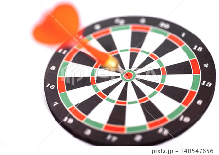 Dart with orange flight embedded in the bullseye of a black and white dartboard, featuring red and green segments, isolated on a white background Dart with orange flight embedded in the bullseye of a black and white dartboard, featuring red and green segments, isolated on a white background 140547656