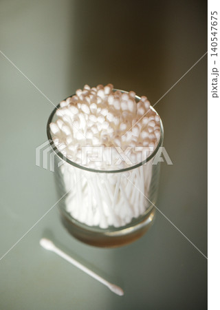 Glass container filled with cotton swabs on a smooth surface, one cotton swab placed beside the container, soft lighting enhances the clean appearance Glass container filled with cotton swabs on a smooth surface, one cotton swab placed beside the container, soft lighting enhances the clean appearance 140547675