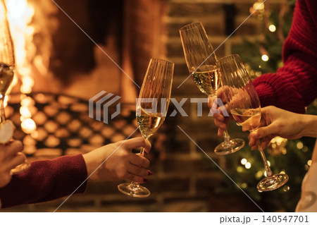 Group of friends toasting with champagne flutes in front of a cozy fireplace decorated for the holiday season, warm lighting and festive atmosphere visible 140547701