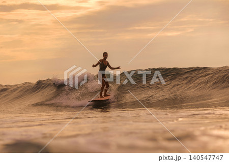 Golden Hour Female Surfer Maintains Steady Stance On Surfboard 140547747
