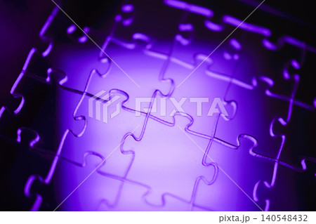 Close-up view of interlocking puzzle pieces illuminated with purple light, showcasing the unique shapes and contours of each piece against a soft background Close-up view of interlocking puzzle pieces illuminated with purple light, showcasing the unique shapes and contours of each piece against a soft background 140548432