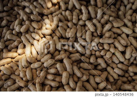 Raw peanuts in their shells scattered on a surface with natural lighting highlighting the texture and color of the nuts in a close-up view Raw peanuts in their shells scattered on a surface with natural lighting highlighting the texture and color of the nuts in a close-up view 140548436