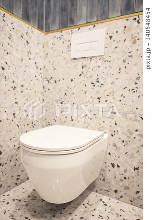 Modern wall-mounted toilet with sleek design installed in a bathroom featuring textured terrazzo flooring and decorative wall tiles in a contemporary setting 140548454