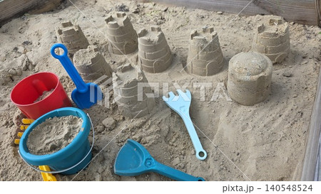 Close up of colorful plastic toys and built sandcastles inside wooden sandbox on foreground, concept of happy childhood and creative outdoor summer games Close up of colorful plastic toys and built sandcastles inside wooden sandbox on foreground, concept of happy childhood and creative outdoor summer games 140548524