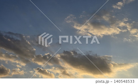 Dark fluffy clouds illuminated by golden sunlight against bright blue sky background, concept of majestic sunset atmosphere and natural beauty 140548533