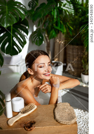 Happy young Caucasian woman smiling while taking a bubble bath in a bright home bathroom Happy young Caucasian woman smiling while taking a bubble bath in a bright home bathroom 140548690
