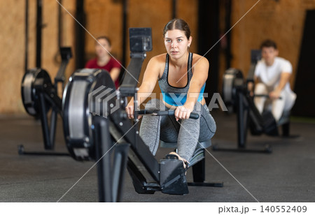 Focused girl works out with rowing machine during class at fitness club Focused girl works out with rowing machine during class at fitness club 140552409