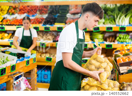 Concentrated male seller stacking up mesh bag with potatoes in shop Concentrated male seller stacking up mesh bag with potatoes in shop 140552662