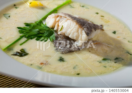 Tasty creamy soup with white fish hake and greens at plate 140553004
