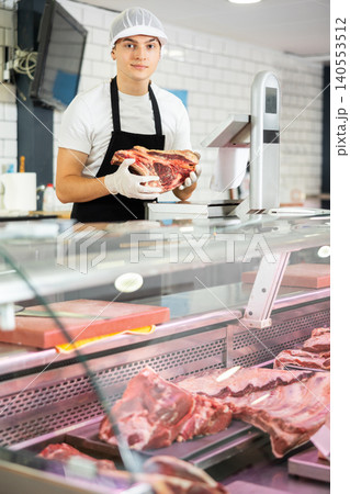 Positive young salesman demonstrating piece of meat in butcher shop 140553512