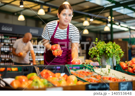 European female seller in apron takes tomatoes from window European female seller in apron takes tomatoes from window 140553648