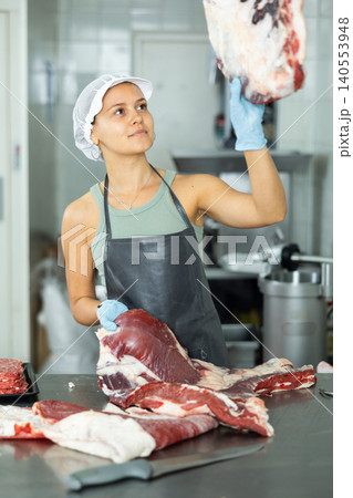 Positive young saleswoman demonstrating piece of meat in butcher shop Positive young saleswoman demonstrating piece of meat in butcher shop 140553948